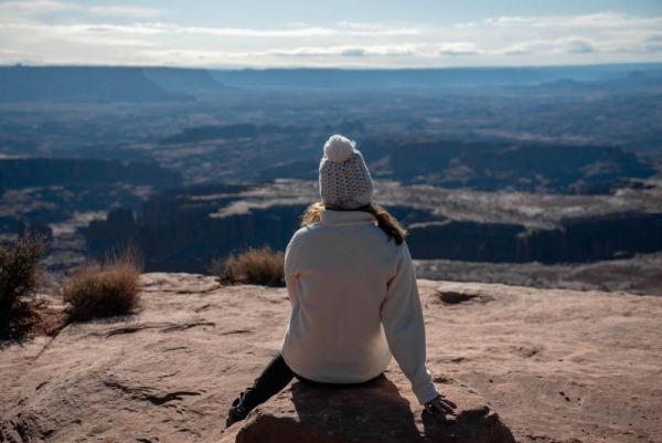 girl in white jacket and hat overlooks grand viewpoint trail in Canyonlands National Park in Utah in winter