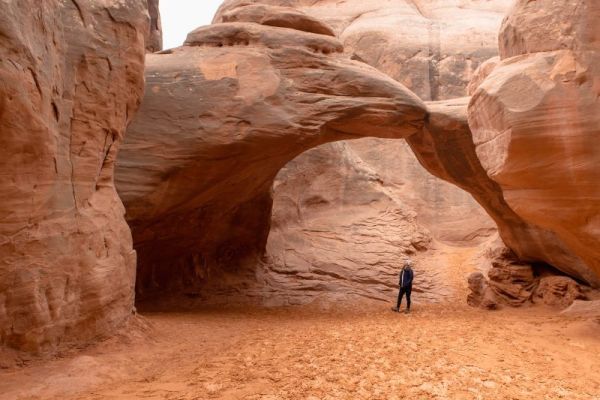 girl looking up at sand dune arch in winter in Arches National Park