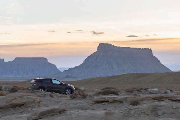 A purple car in front of factory butte in Utah at sunset