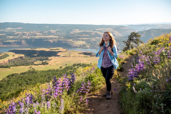 girl in purple and blue shirt and hiking clothes hiking in the columbia river gorge during wildflower season