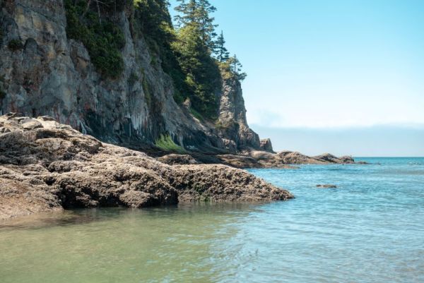 view of rocky cliffs with sandy beach and the Pacific Ocean reaching the base