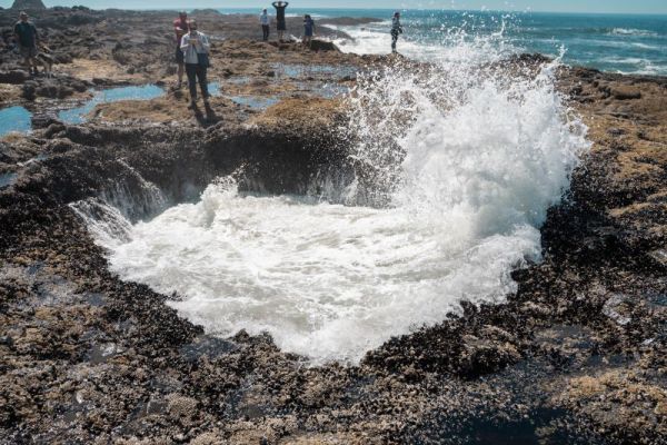 Thor's Well at low tide, with waves crashing in and visitors onlooking