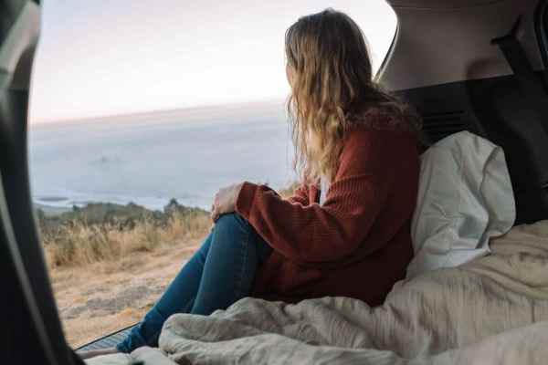 girl in red cardigan and jeans sitting in her car looking at the Oregon Coast