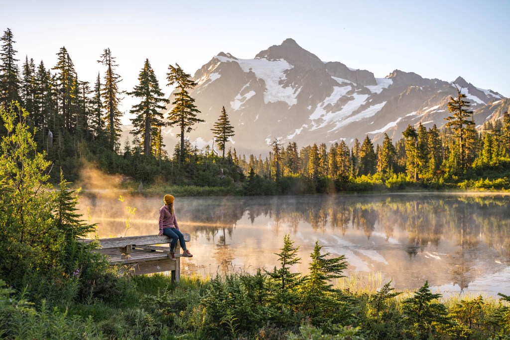 woman in pink jacket and yellow hat hiking to a mountain lake in washington