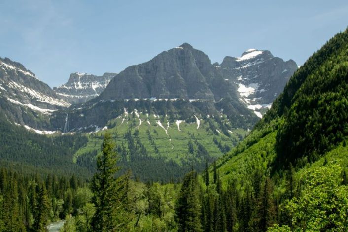 mountains with grass and trees at base and topped with snow in spring in Glacier National Park