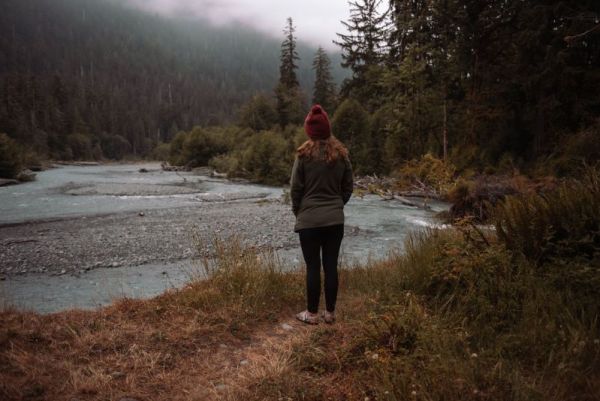 girl in green fleece and red hat looking out at misty clouds over the Hoh River