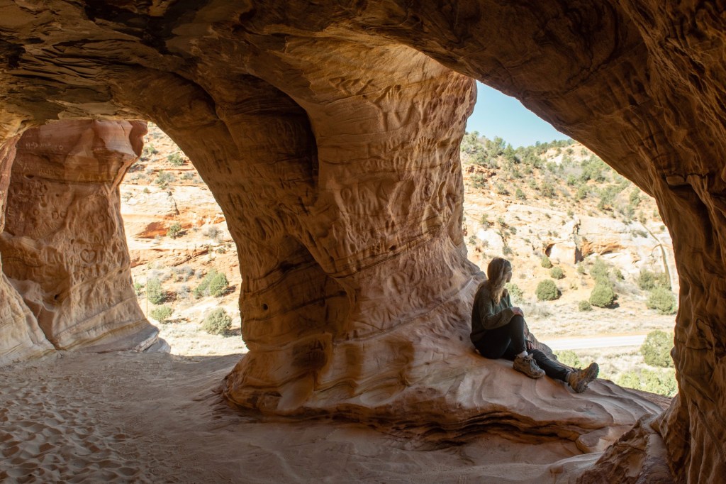 girl in Moqui Caverns sitting in the Sand Caves near Kanab, Utah looking out