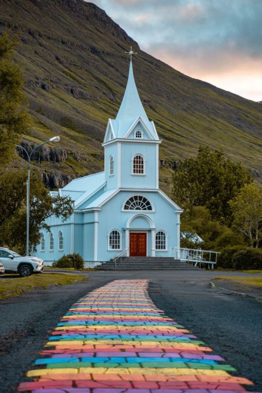 rainbow road leading up to a pale blue church in Iceland