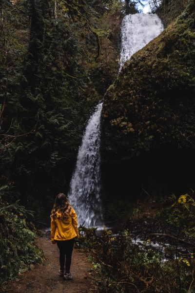 girl in yellow jacket looking up at Upper Latourell Falls in Oregon's Columbia River Gorge