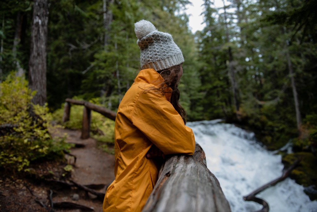 Girl in yellow jacket looking at Mudcap falls in Mount Rainier National Park 