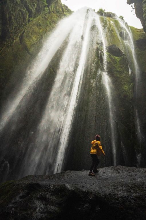 view in canyon of girl in yellow jacket looking up at waterfall