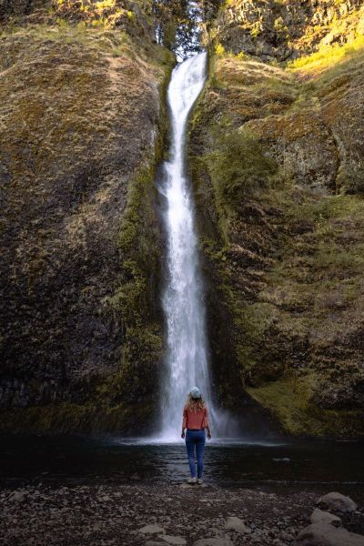 girl in orange shirt standing in front of Horsetail Falls in the Columbia River Gorge on an Oregon road trip