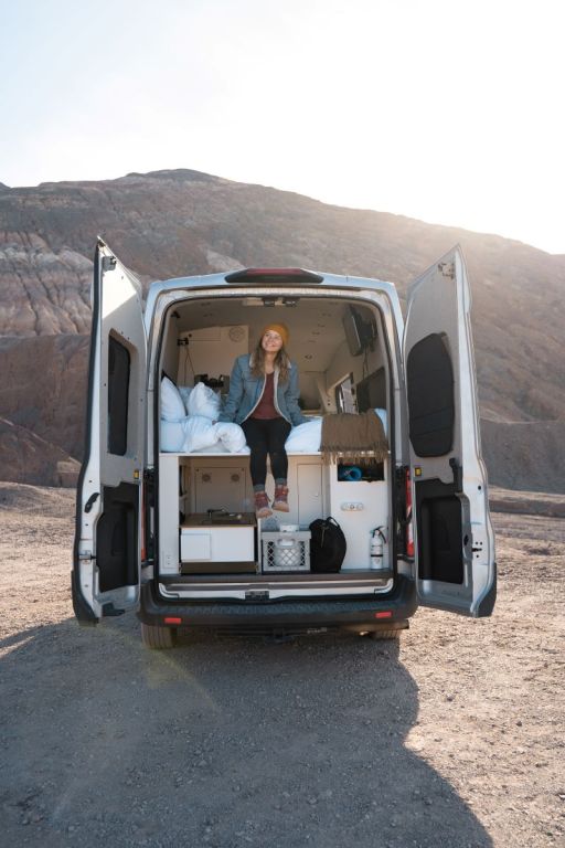 girl in campervan in the desert looking out at the mountains with the doors open